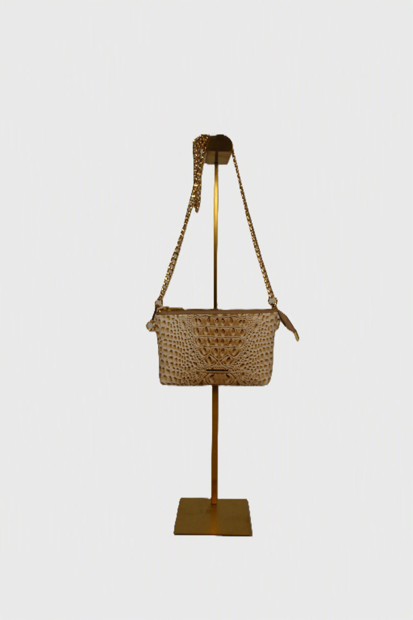 Sand Dune Croc Crossbody Bag with gold chain strap on a gold display stand