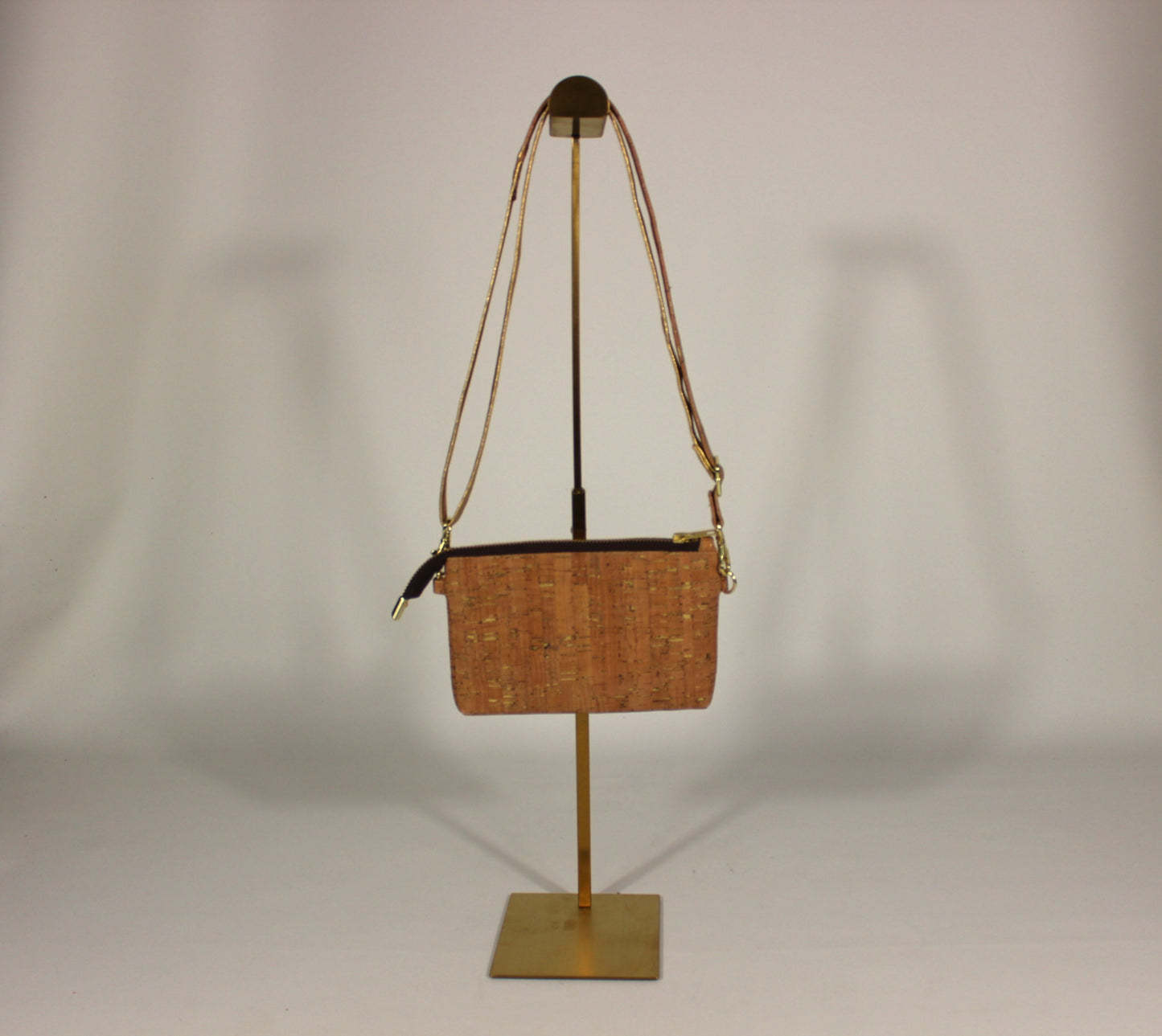 Cork Crossbody Bag with natural grain texture and gold hardware on a gold display stand