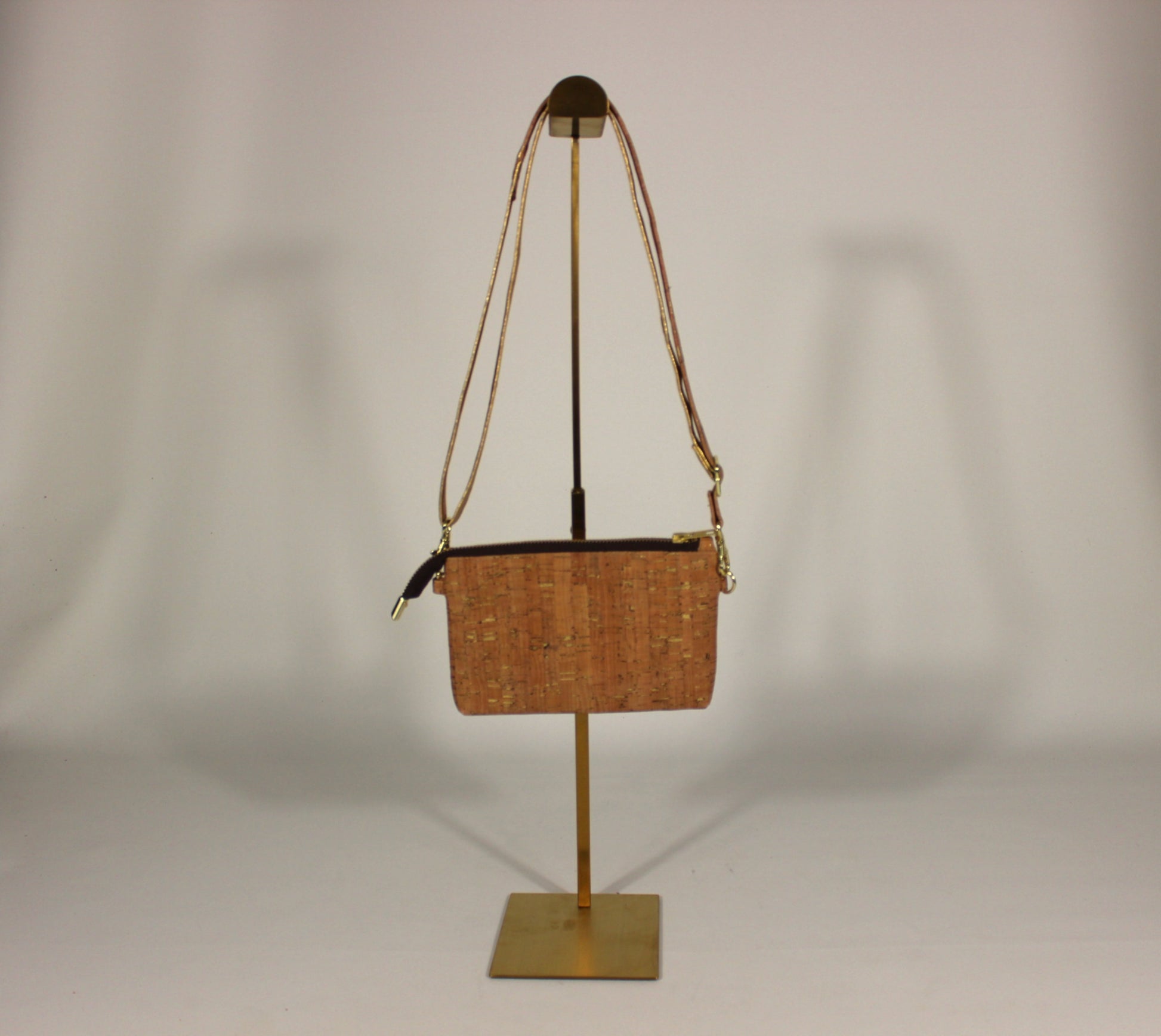 Cork Crossbody Bag with natural grain texture and gold hardware on a gold display stand